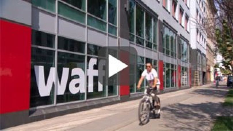 copyright: Popup TV und Film Produktion GmbH Screenshot einer Videoeinstellung: Eine Fahrradfahrerin fährt am waff-Gebäude vorbei.