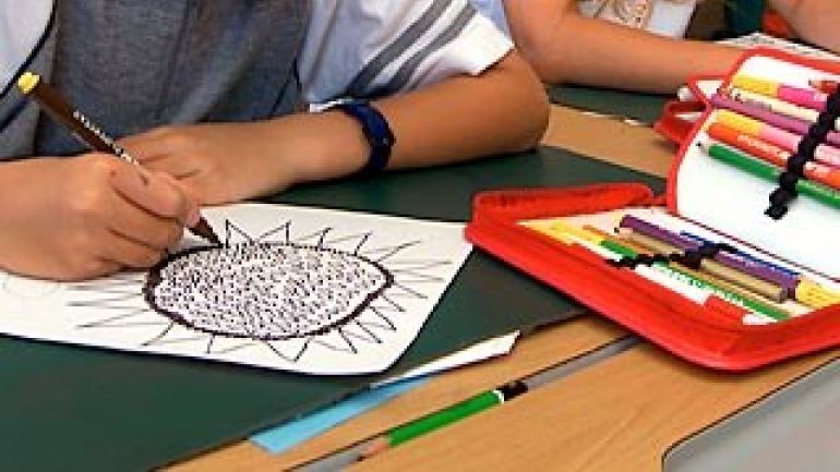 Schüler zeichnet ein Bild, daneben Buntstifte