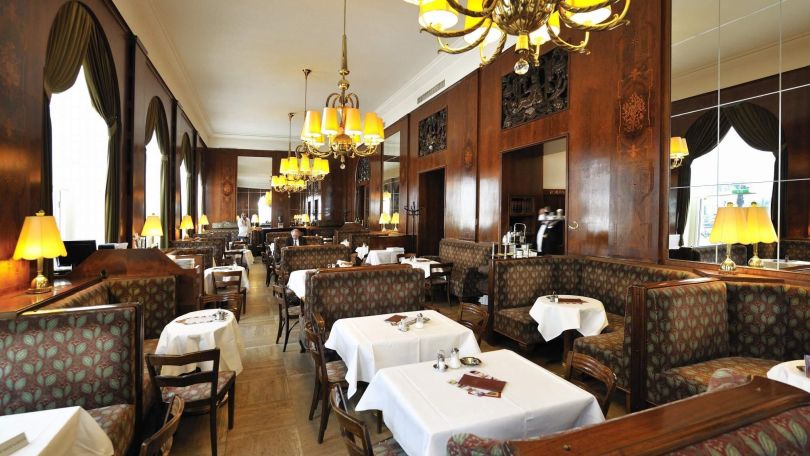 Innenraum eines traditionellen Wiener Kaffeehauses mit dunkler Holzvertäfelung, braunen Polstersesseln und weißen Tischtüchern.