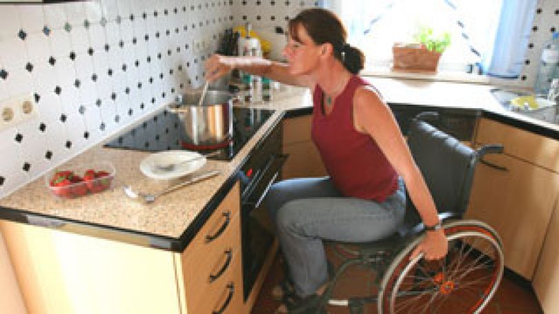 Frau im Rollstuhl kocht.