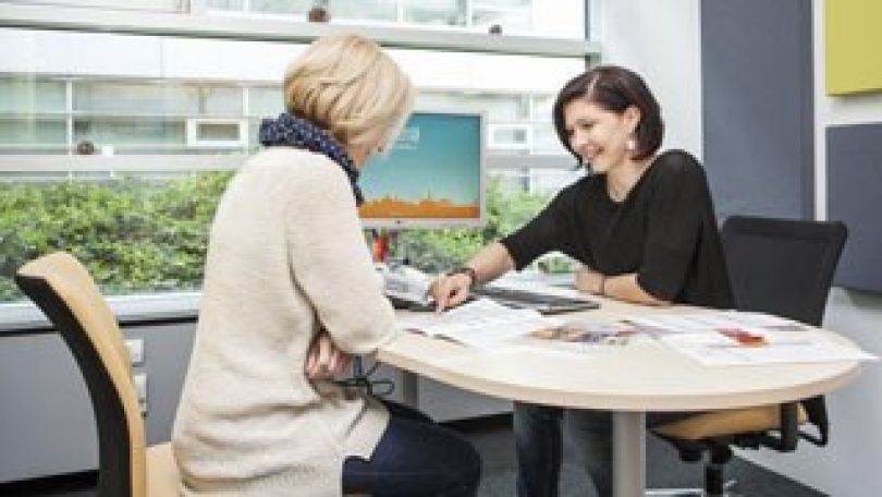 Eine Beraterin sitzt beim Schreibtisch und berät eine Kundin