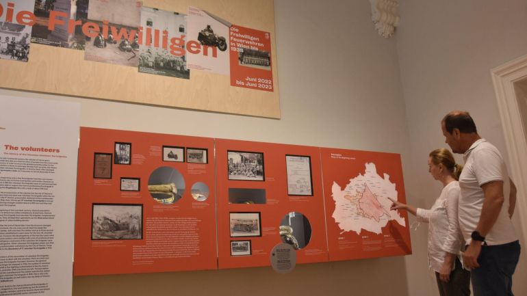 2 Menschen sehen sich die Schautafeln einer Ausstellung an