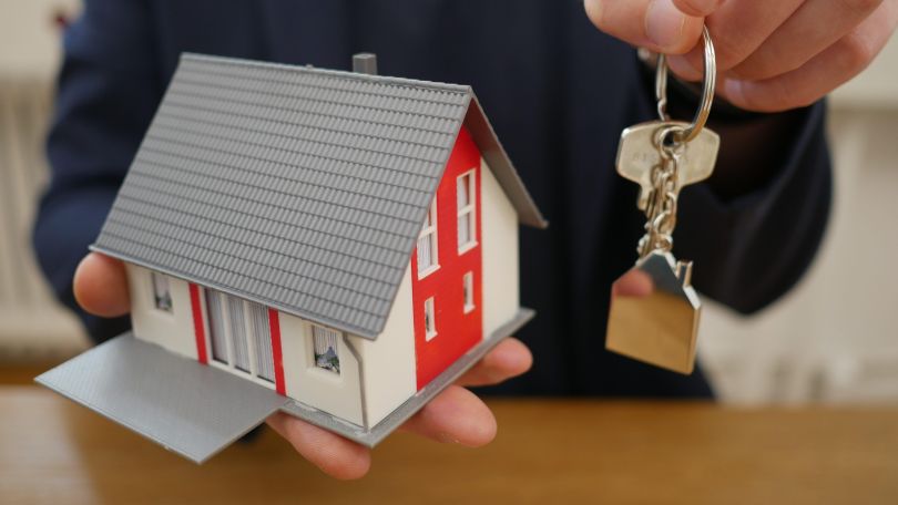 Eine Person hält ein Miniaturhaus und einen Schlüssel