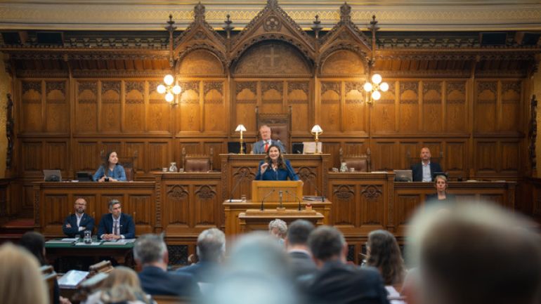 Stadträtin Novak hält im Gemeinderat eine Rede. Sie steht im holzgetäfelten Saal an einem Rednerpult.