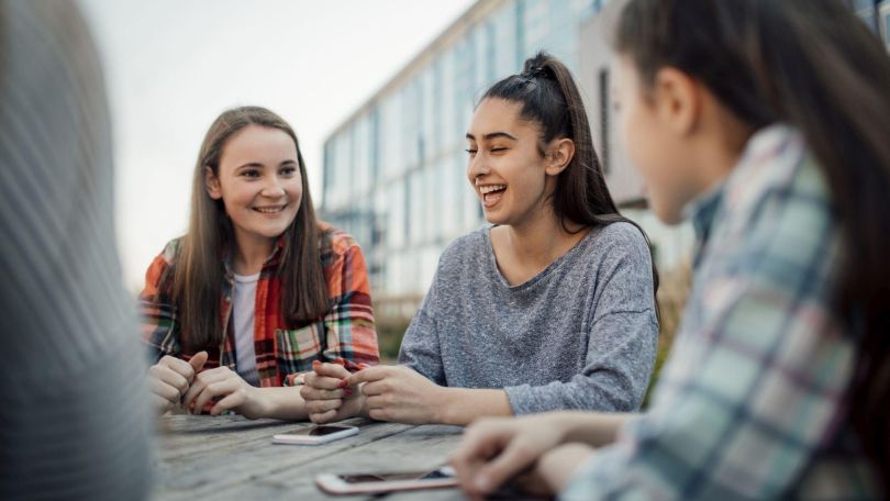 copyright: Getty Images Eine Gruppe junger Frauen sitzt bei einem Tisch und unterhält sich vergnügt.