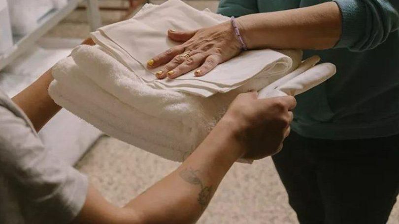 Frau gibt einer anderen Person mehrere Handtücher.