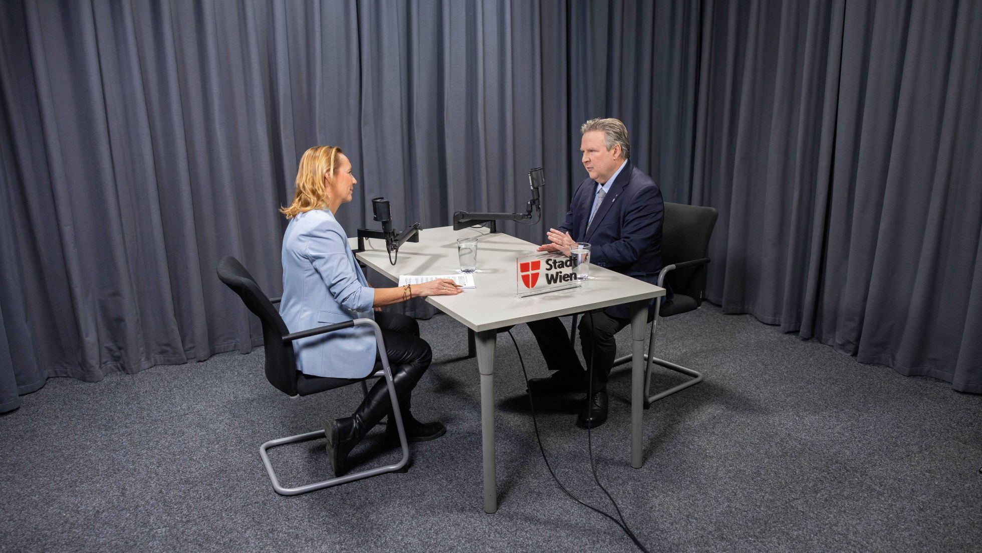 Bürgermeister sitzt an einem Tisch mit einer Dame und führt ein Interview