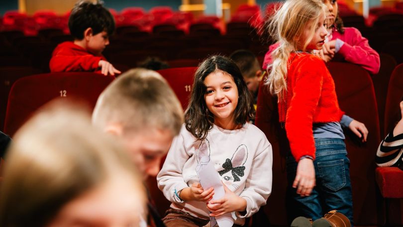 copyright: Aleksandra Kawka Eine Kindergruppe spielt in einem leeren Kinosaal. Ein Mädchen hält einen Zettel in der Hand und lächelt in die Kamera.