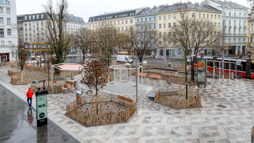 Platz mit Bäumen und Beeten, Wasserspiel und Sitzgelegenheiten
