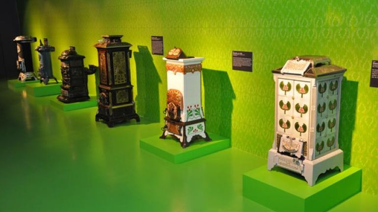 copyright: MA 34 - Bau- und Gebäudemanagement Several stoves in a row, displayed in a green room.