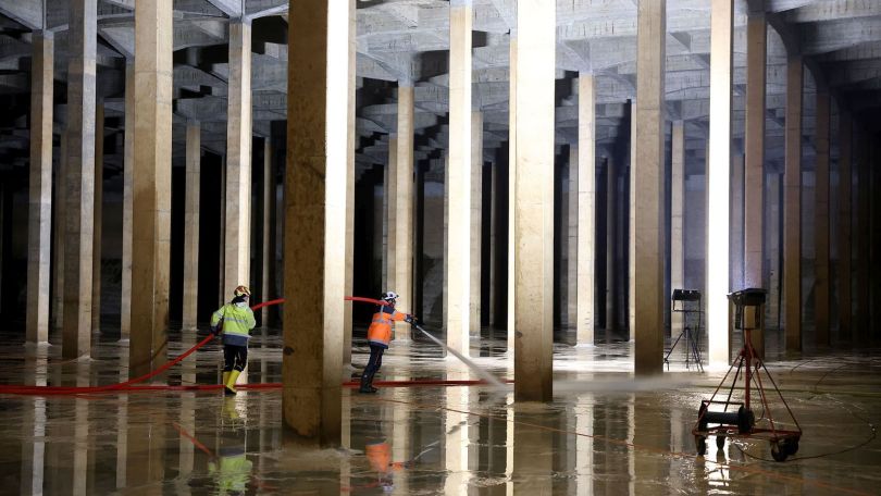 Großer unterirdischer Wasserbehälter aus Beton mit Säulen und Mitarbeitern, die mit Wasserschlauch arbeiten.