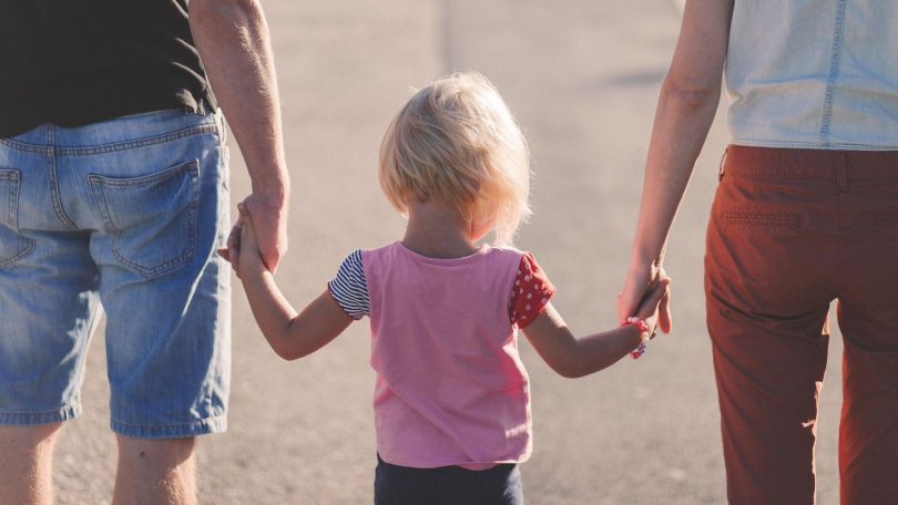 Mutter und Vater gehen Hand in Hand mit Kleinkind eine Allee entlang