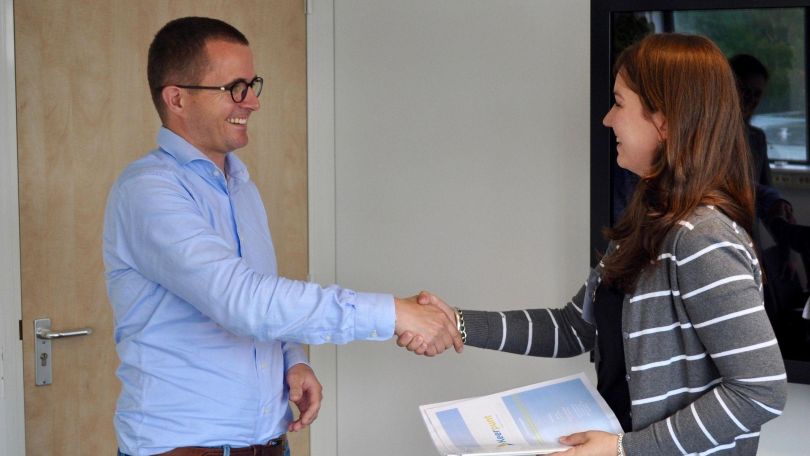 Mann und Frau mit Unterlagen schütteln Hände und lächeln sich dabei an