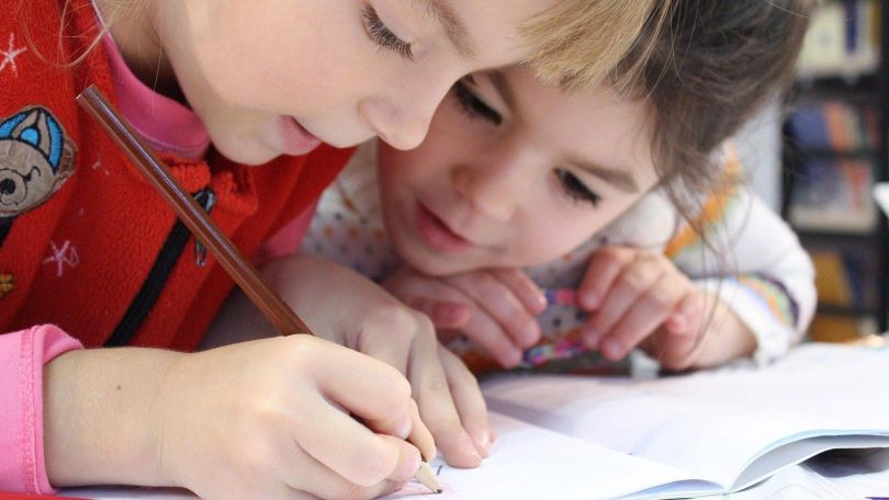 Two pupils are bent over a notebook writing