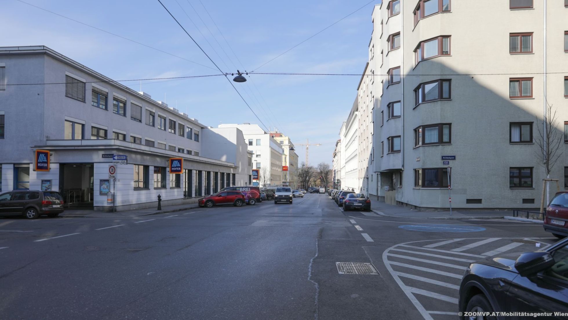 copyright: ZOOM.AT/Mobilitätsagentur Wien Straße und daneben parkende Autos und ein paar niedrigere und ein paar höhere Wohngebäude.
