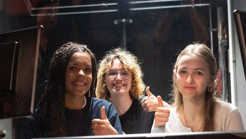 3 Mädchen sitzen im Technikraum eines Theaters und zeigen den Daumen hoch.