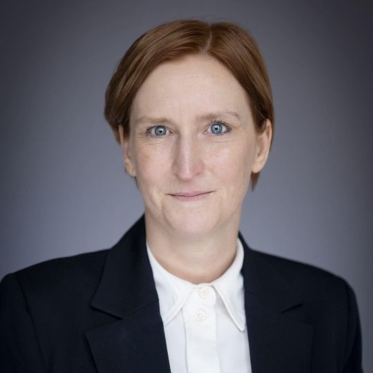 Frau mit hellbraunen kürzeren Haaren und blauen Augen, schwarzem Blazer und weißer Bluse
