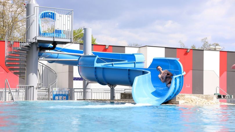 Junge Frau rutscht auf einer blauen Rutsche ins Schwimmbecken.