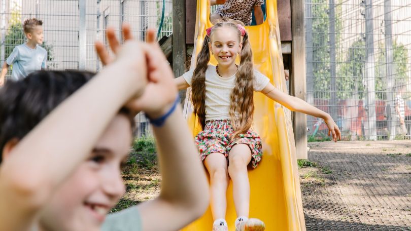 Ein Mädchen rutscht am Spielplatz eine gelbe Rutsche hinunter.