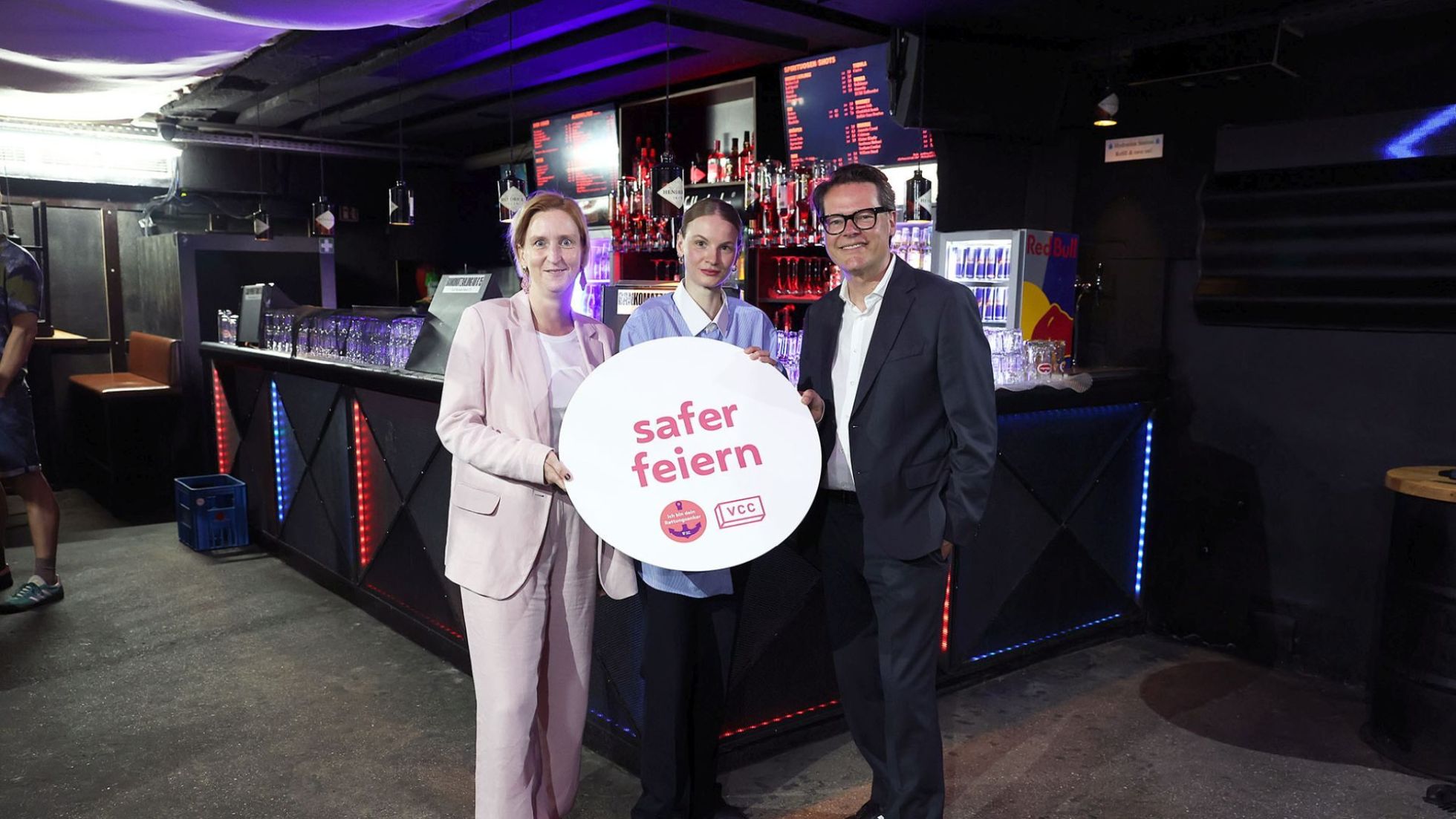 copyright: Stadt Wien/Martin Votava 2 Politikerinnen und ein Politiker in einem Club halten ein rundes Schild "safer feiern".