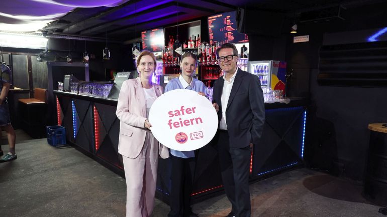 copyright: Stadt Wien/Martin Votava 2 Politikerinnen und ein Politiker in einem Club halten ein rundes Schild "safer feiern".