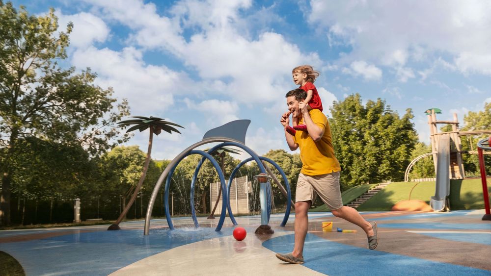 Ein Mann läuft mit einem Kleinkind auf den Schultern über einen Wasserspielplatz