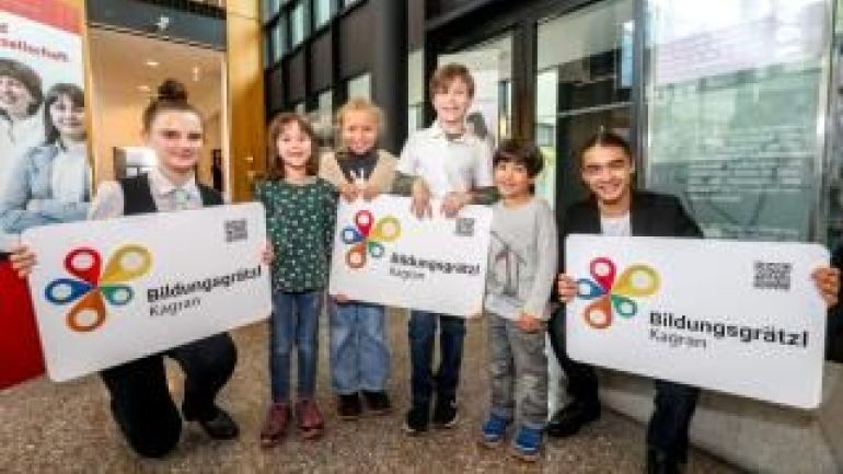 copyright: Christian Fürthner 5 Kinder und 1 erwachsene Person halten 3 Schilder mit der Aufschrift "Bildungsgrätzl"