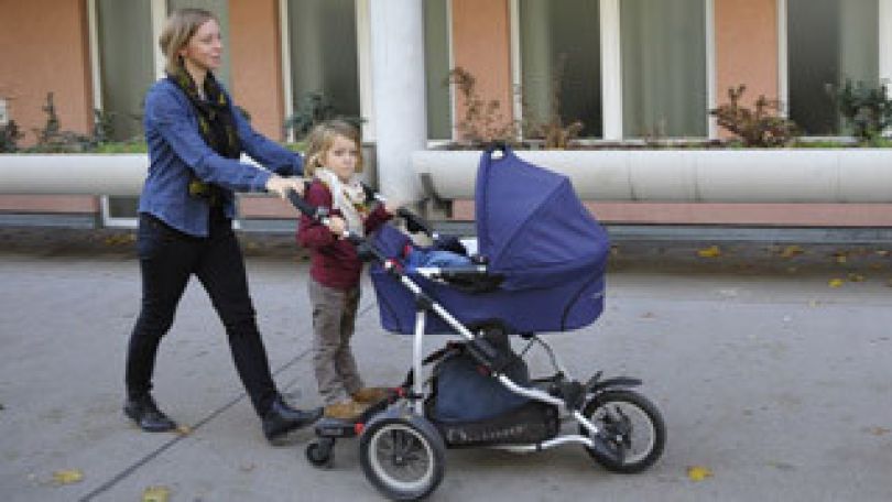 Eine Mutter schiebt mit Kind einen Kinderwagen.