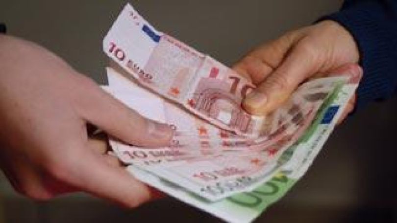 Gldscheine werden von einer Hand in die andere gereicht.