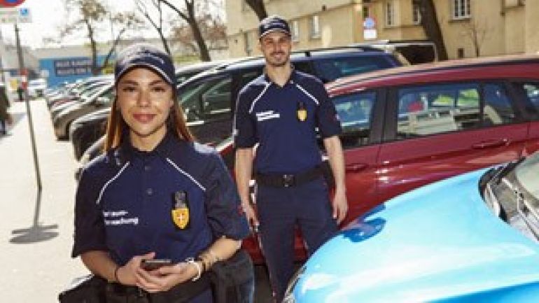 Parkwächterin und Parkwächter zwischen parkenden Autos