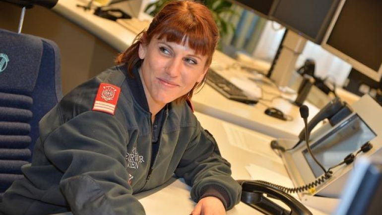 Eine Feuerwehrfrau in einem Kontrollraum mit Telefonen und Monitoren