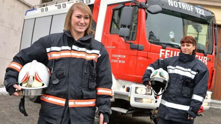 Zwei Feuerwehrfrauen stehen in Montur vor einem Feuerwehrauto
