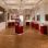 copyright: Stadt Wien - Feuerwehr Historischer Ausstellungsraum im Wiener Feuerwehrmuseum mit Parkettboden, Kronleuchtern und Gemälden an den Wänden. Mehrere rote Vitrinen präsentieren Exponate und Informationstafeln in einem hellen Museumsraum.