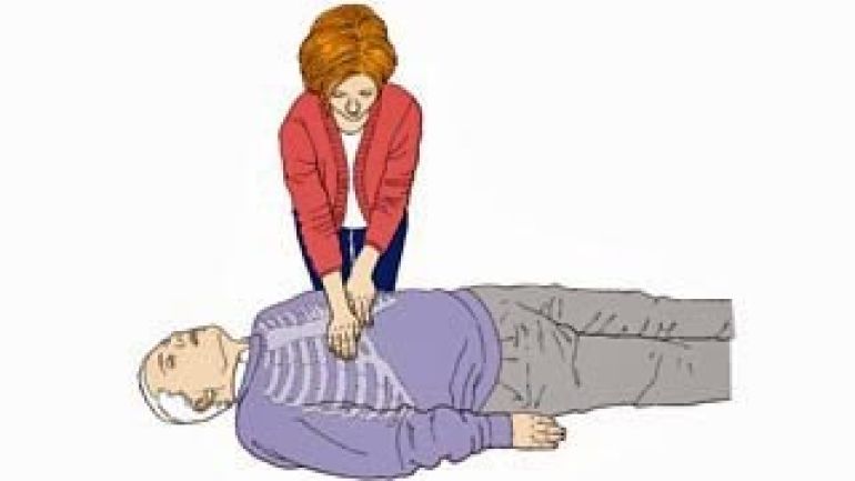 Eine Frau sucht bei einer liegenden Person den Druckpunkt für eine Herzdruckmassage.