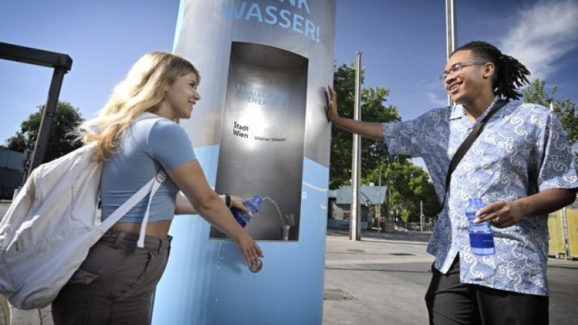 2 Menschen stehen vor einem Trinkwasserbrunnen.
