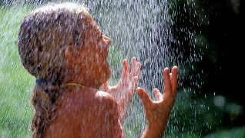 Mädchen steht unter einer Wasserdusche im Freien