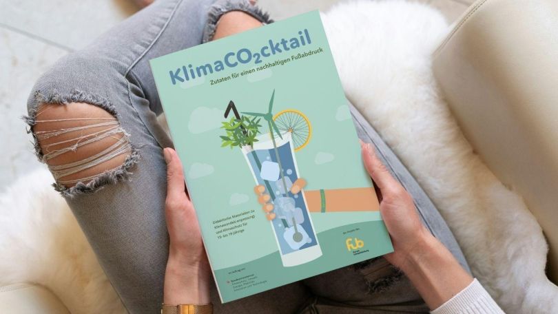 copyright: Forum Umweltbildung / Christoph Rossmeissl Jemand hält das Buch "Klimaco2cktail" am Schoß