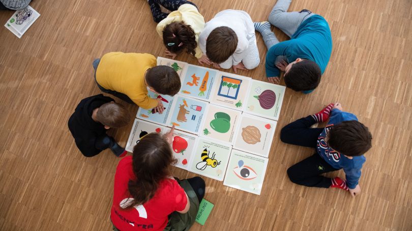 Kinder sitzen am Boden und schauen sich große Karten mit bunten Bildern an