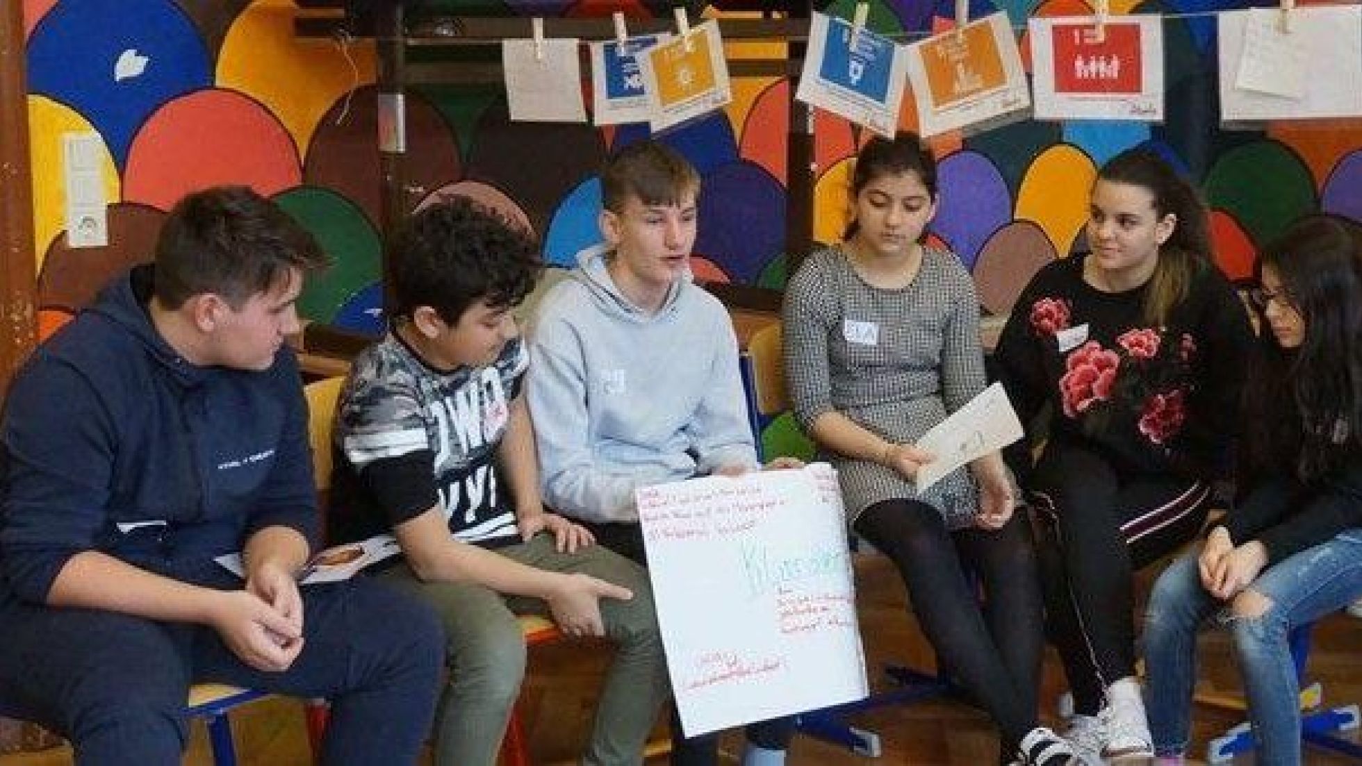 Eine Gruppe Jugendlicher sitzt im Halbkreis und ein Bursche hält ein Plakat hoch