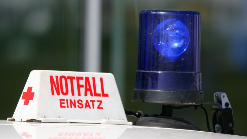 Schild "Notfall-Einsatz" mit rotem Kreuz auf einem Autodach mit Blaulicht