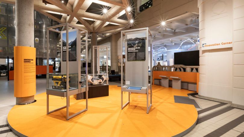 Im Ausstellungsraum ist ein gelber Bereich in dem hohe Vitrinen mit Ausstellungsstücken und Infotexten stehen.