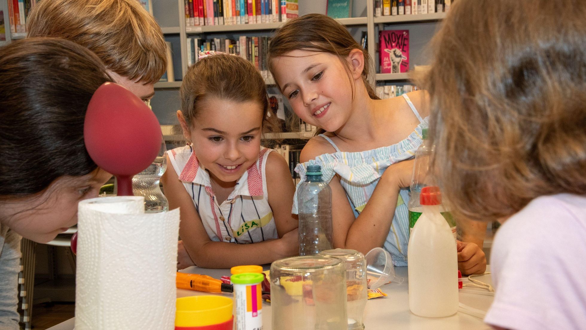 Mehrere Kinder sitzen an einem Tisch auf dem verschiedene Gegenstände zum Basteln stehen.