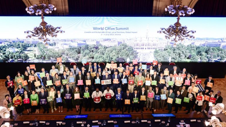 Gruppe von Teilnehmenden vor einem breiten Banner mit "World Cities Summit"