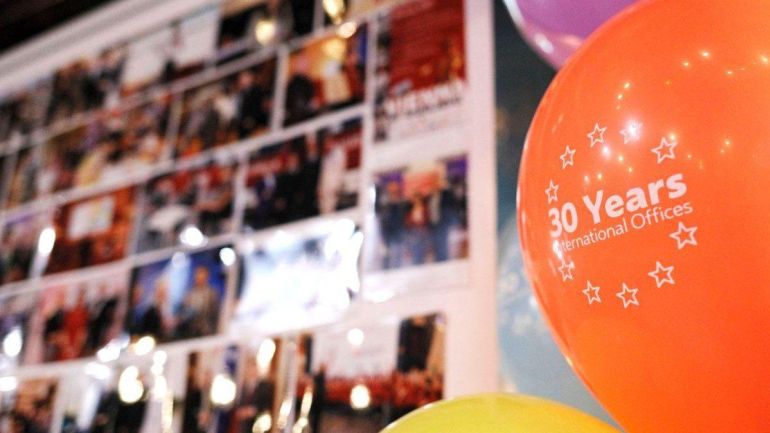copyright: WH International Services/Vanja Čerimagić Oranger Luftballon mit der Aufschrift "30 Years International Offices", im Hintergrund eine Fotowand
