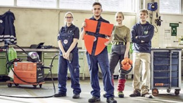 copyright: Robert Staudinger 4 Jugendliche in einer Werkstatt, einer hält ein großes Logo der Stadt Wien