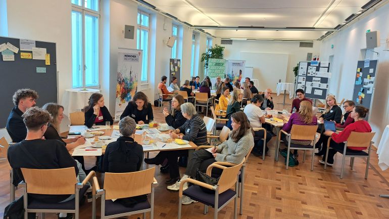 Junge Menschen sitzen in Grüppchen rund um Tische bei Workshop