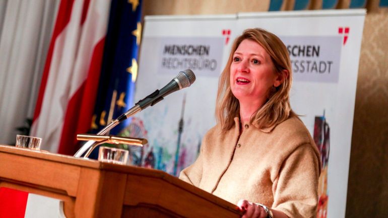 copyright: Stadt Wien/Christian Fürthner Frau mit beiger Jacke und blonden Haaren spricht in ein Mikrofon am Rednerpult.