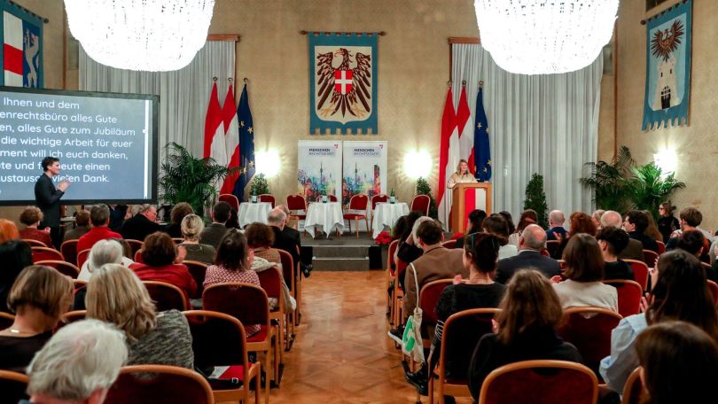 Festlicher Saal mit Wappen an den Wänden, Sesselreihen und kleinem Podium.