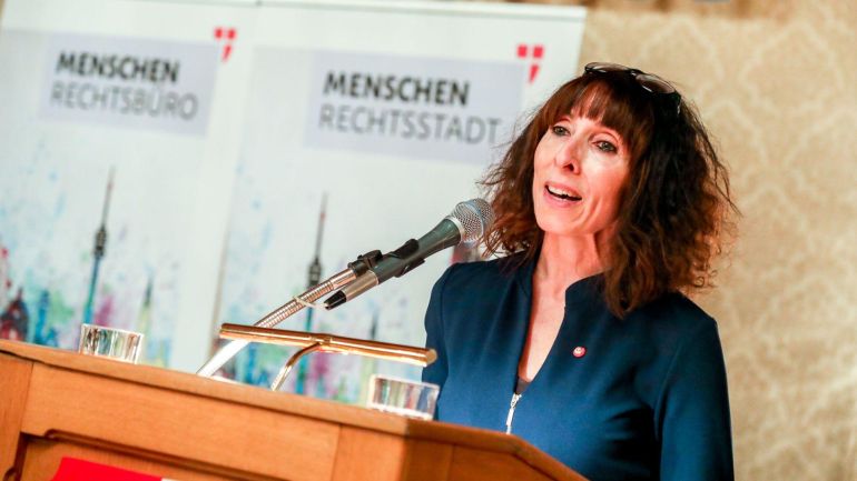 copyright: Stadt Wien/Christian Fürthner Frau mit braunen schulterlangen Locken spricht in ein Mikrofon am Rednerpult.