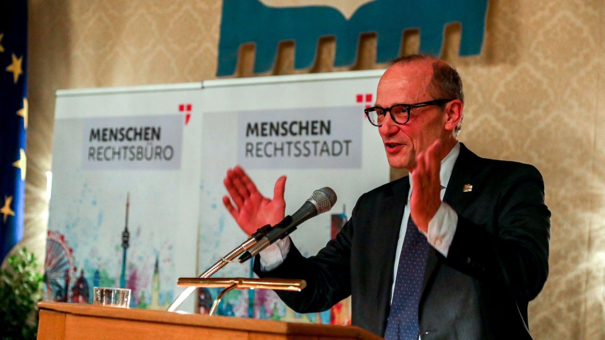copyright: Stadt Wien/Christian Fürthner Ein Mann mit schwarzer Brille und schwarzem Sakko spricht in ein Mikrofon am Rednerpult.